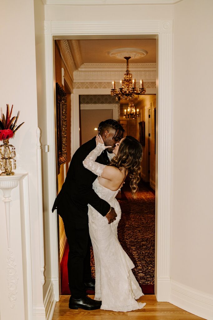 A bride and groom kiss one another while standing in a doorway