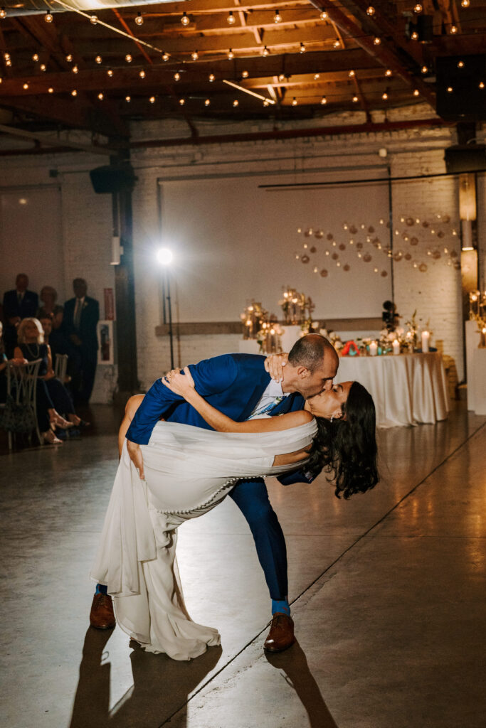 Groom in a blue suit dips his wife in a beautiful white gown for a kiss in the reception room at the Walden Chicago. 