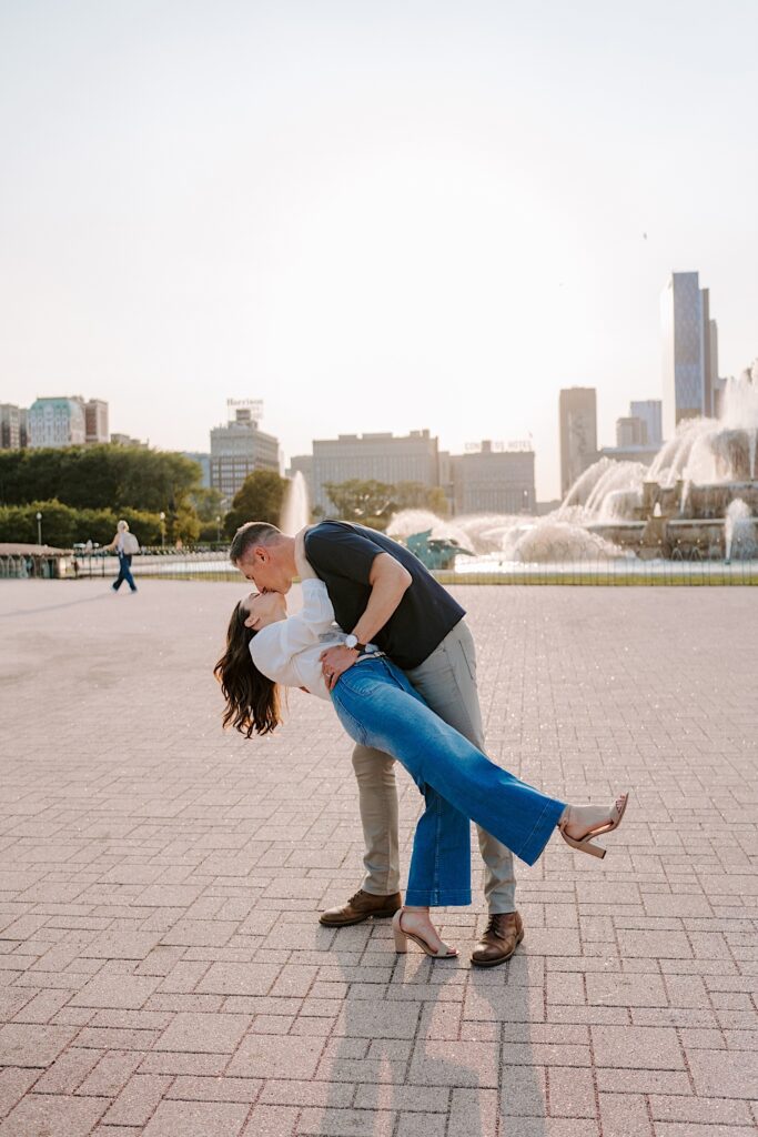 A engaged couple dances in front of Buckingham Fountain in Grant Park Chicago during their engagement session during the summer. 