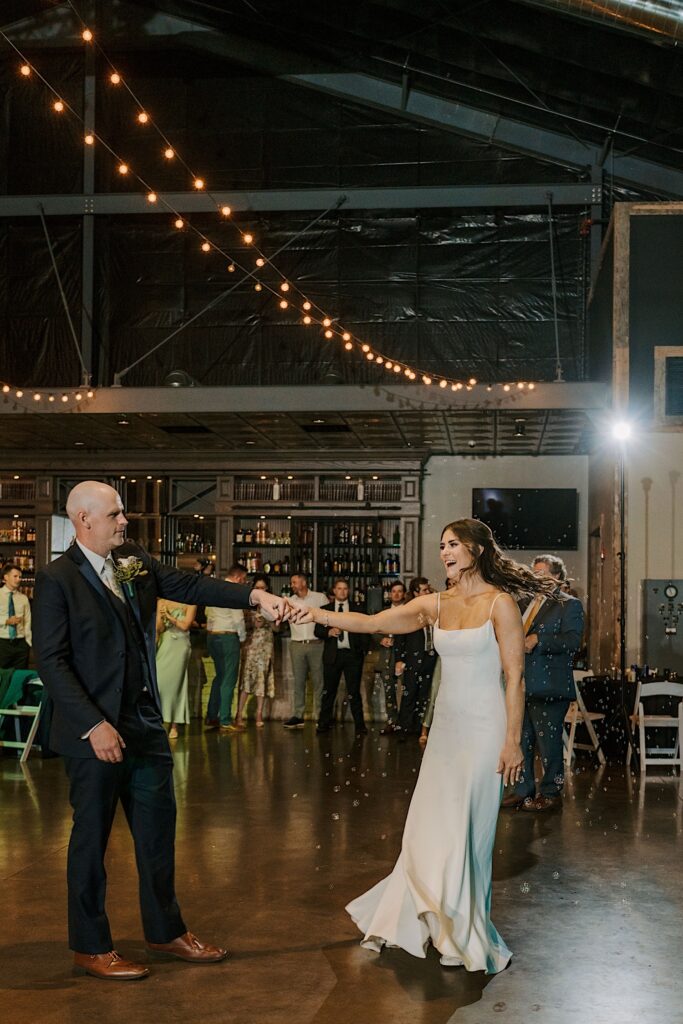 A bride and groom share a first dance at CD&ME an industrial style wedding venue in Frankfort Illinois while a guest uses a bubble machine.